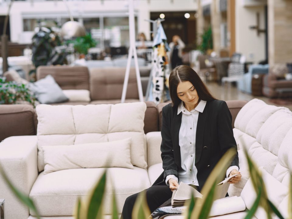Kvinna sitter i en ljus soffa och tittar på tygprover i en möbelbutik